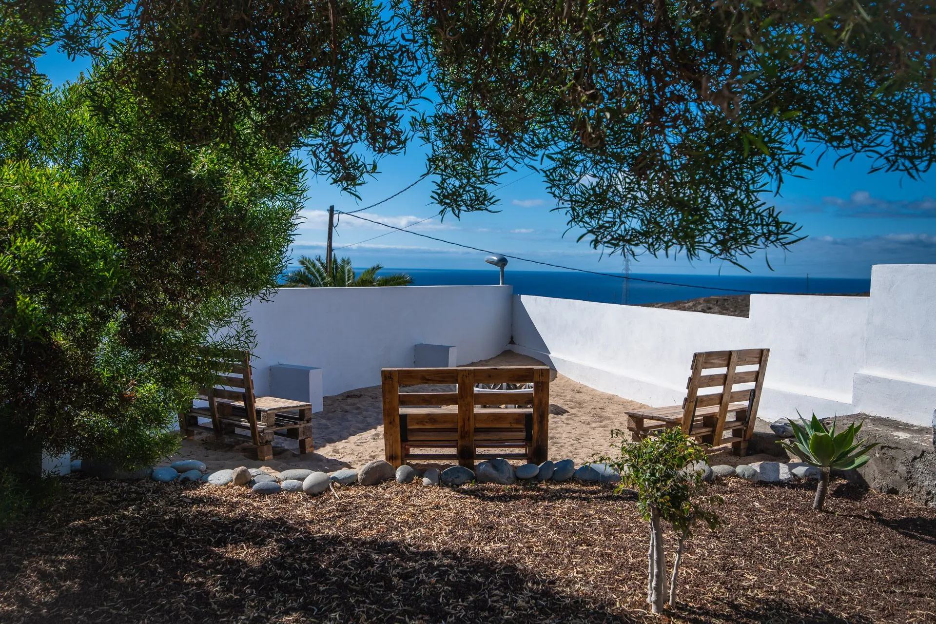 Panche in legno su terrazza con muretti bianchi e vista sul mare