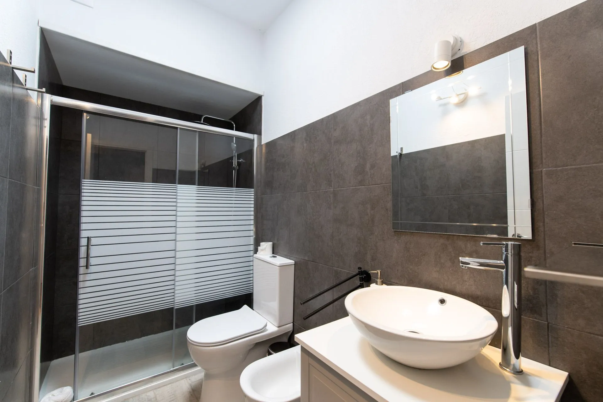Bagno con doccia in vetro, piastrelle scure e lavabo d'appoggio