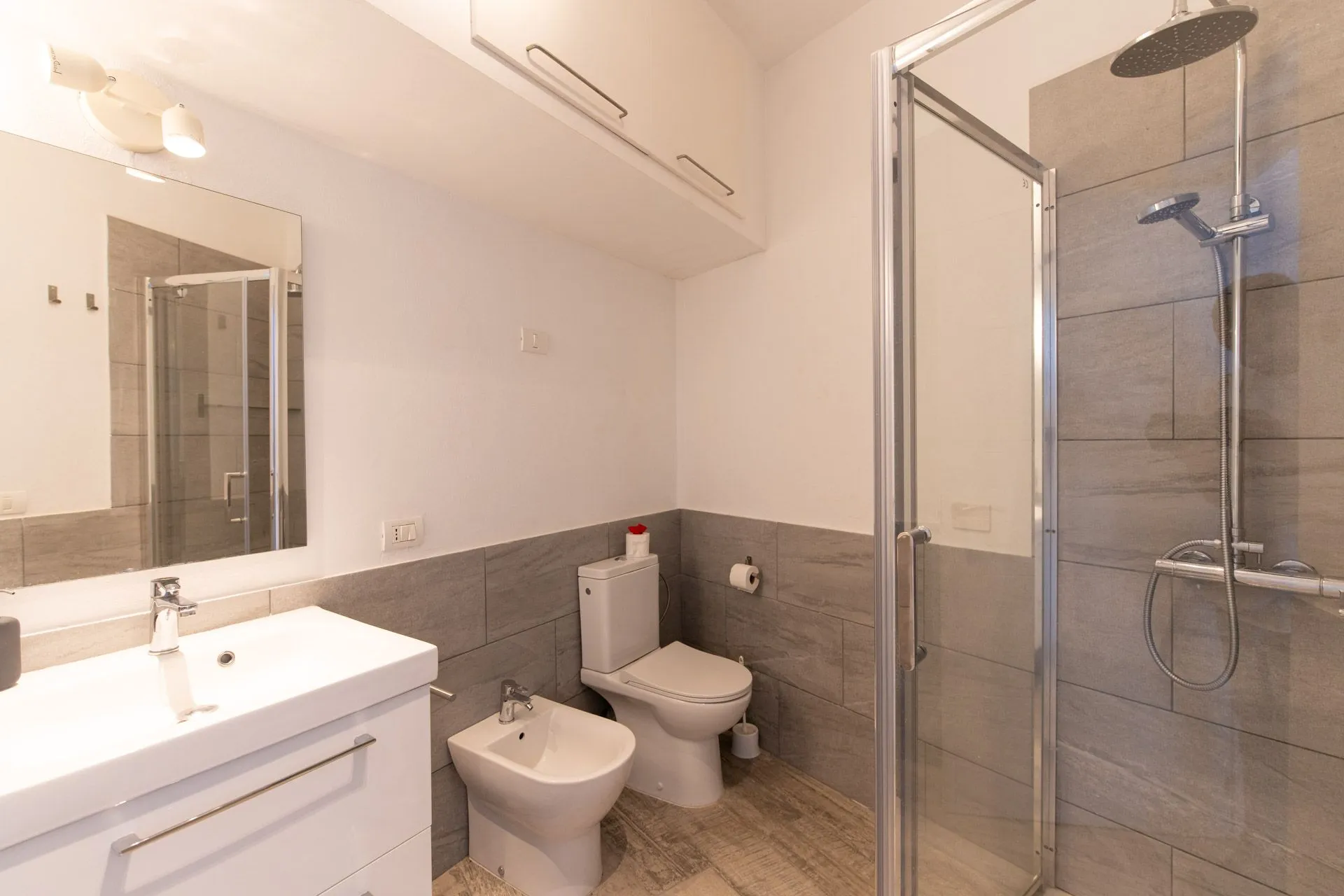 Bagno con doccia in vetro, bidet e wc su pavimento in legno