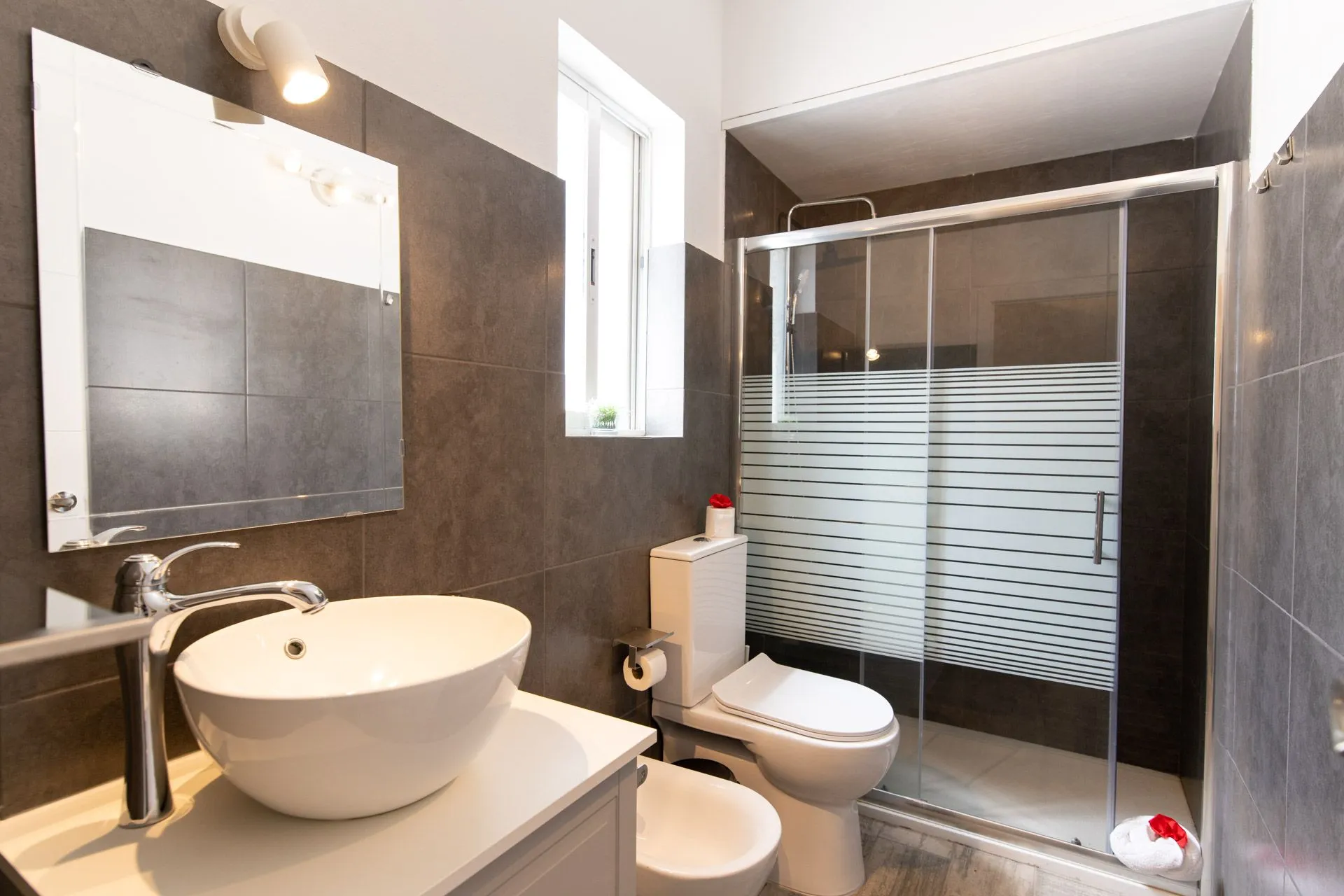 Bagno moderno con doccia in vetro e lavabo d'appoggio su piastrelle scure