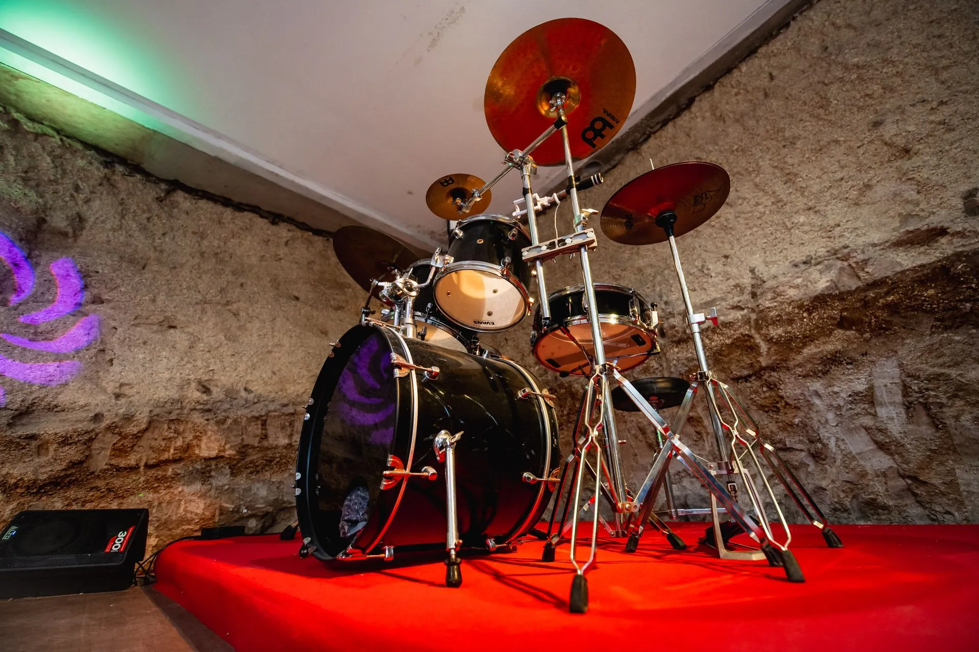 Batteria musicale su palco con tappeto rosso e pareti in pietra