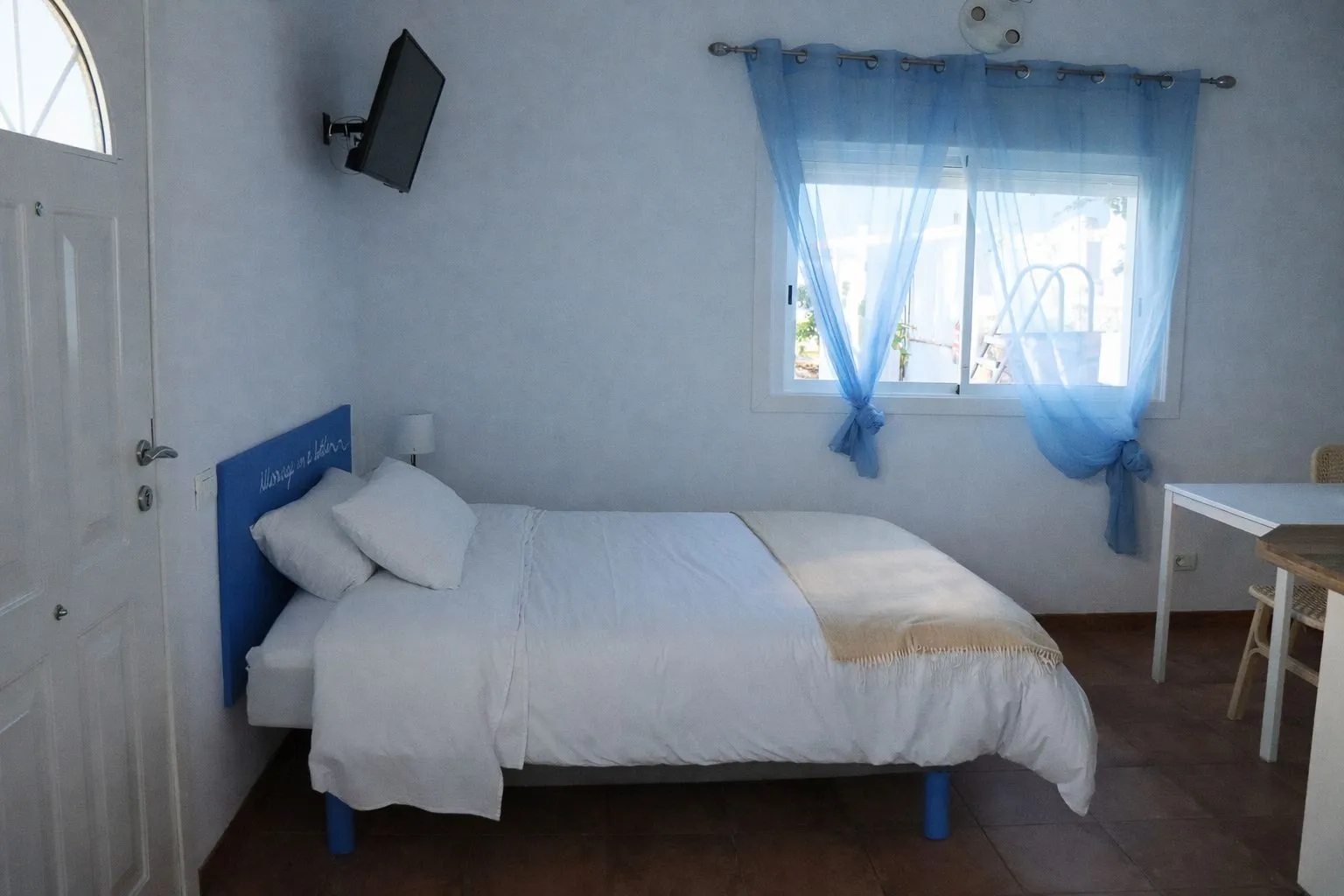 Camera di Casa Sting con testiera blu con scritta, tv a muro e tenda azzurra