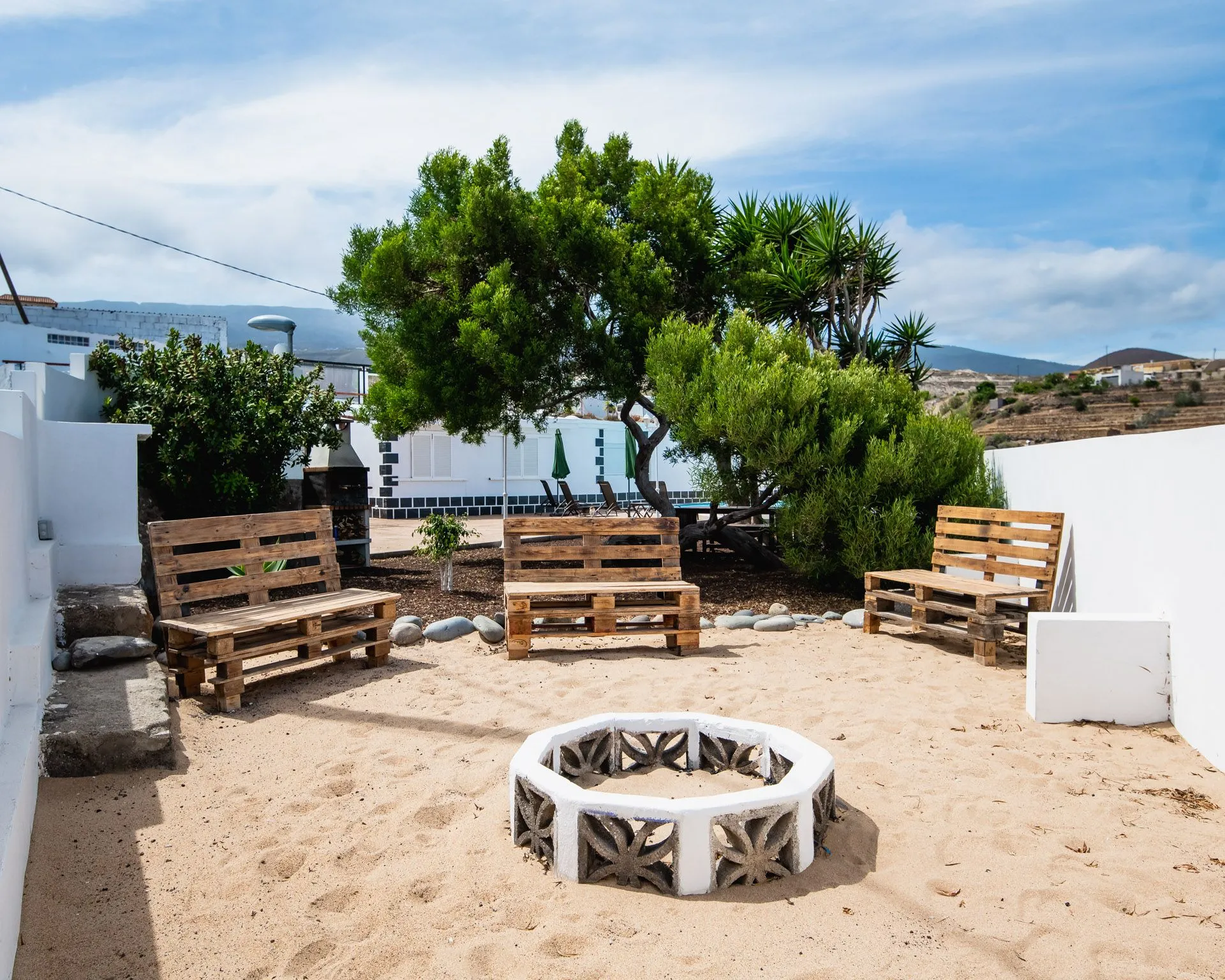 Cortile con panche in legno e falò circondato da sabbia e alberi