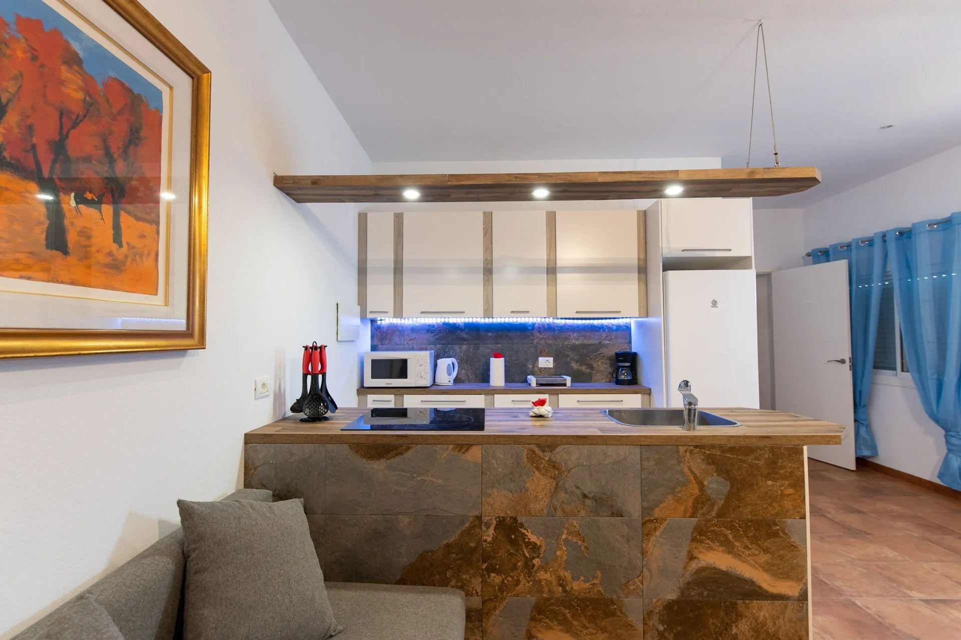 Cucina con isola in pietra, quadro colorato a parete e tende blu