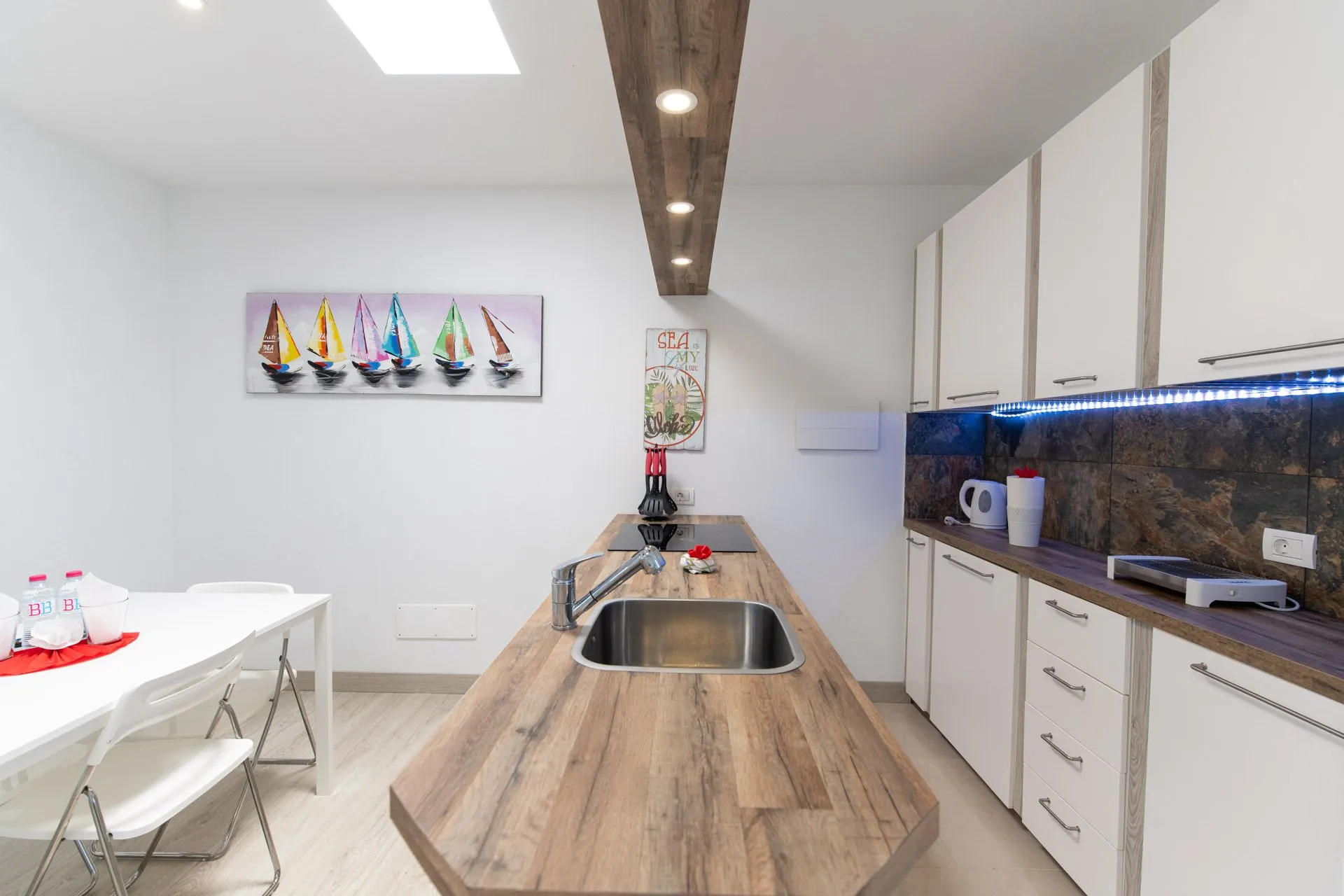 Cucina lineare con isola in legno, travetto a soffitto e quadro di barche a vela