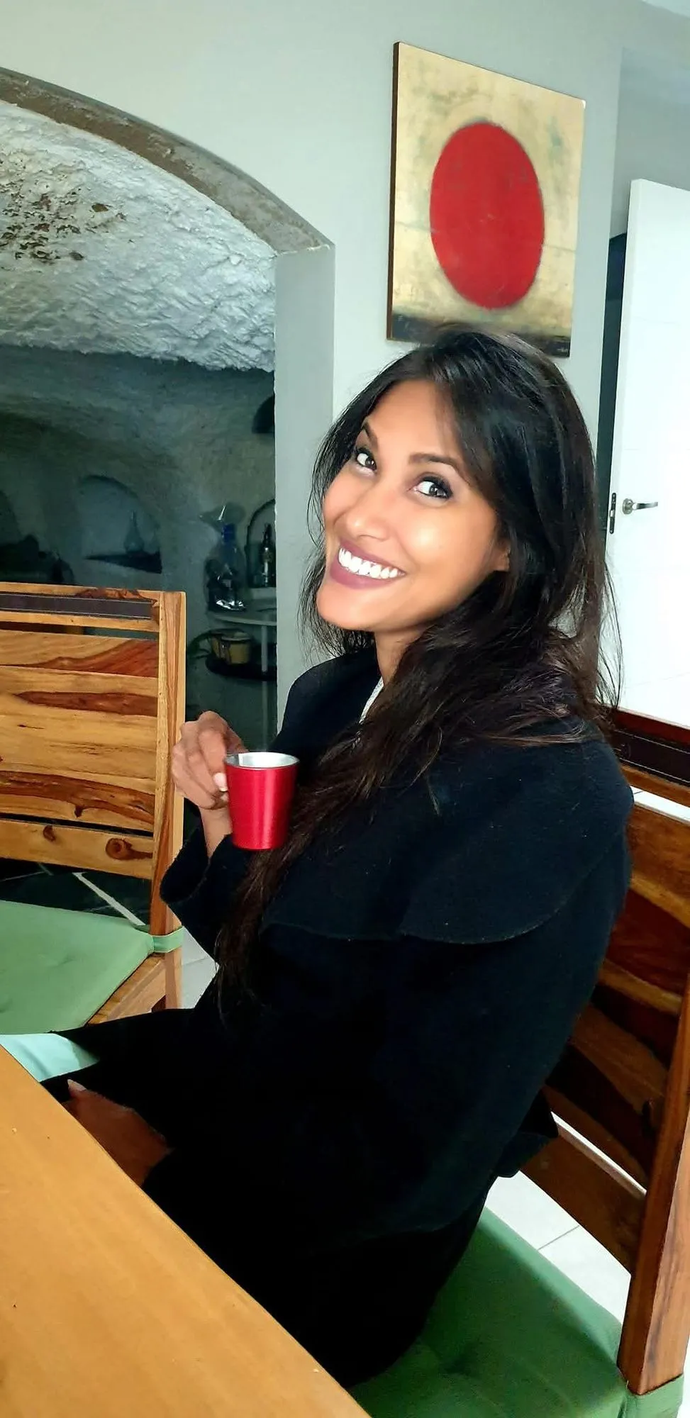 Donna sorridente seduta a tavola con una tazza rossa in mano