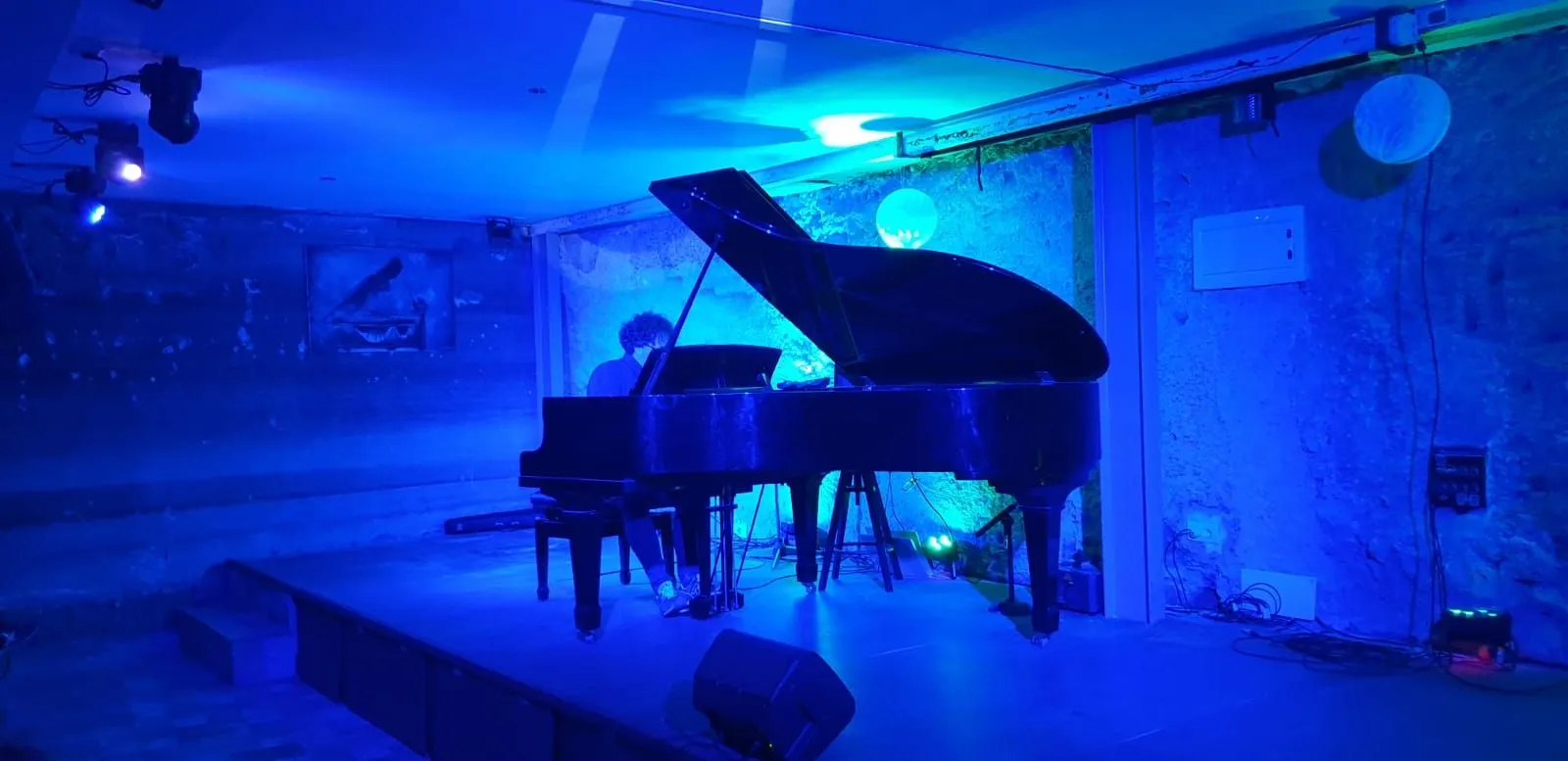 Pianoforte a coda su un palco illuminato di blu in una sala con pareti in pietra