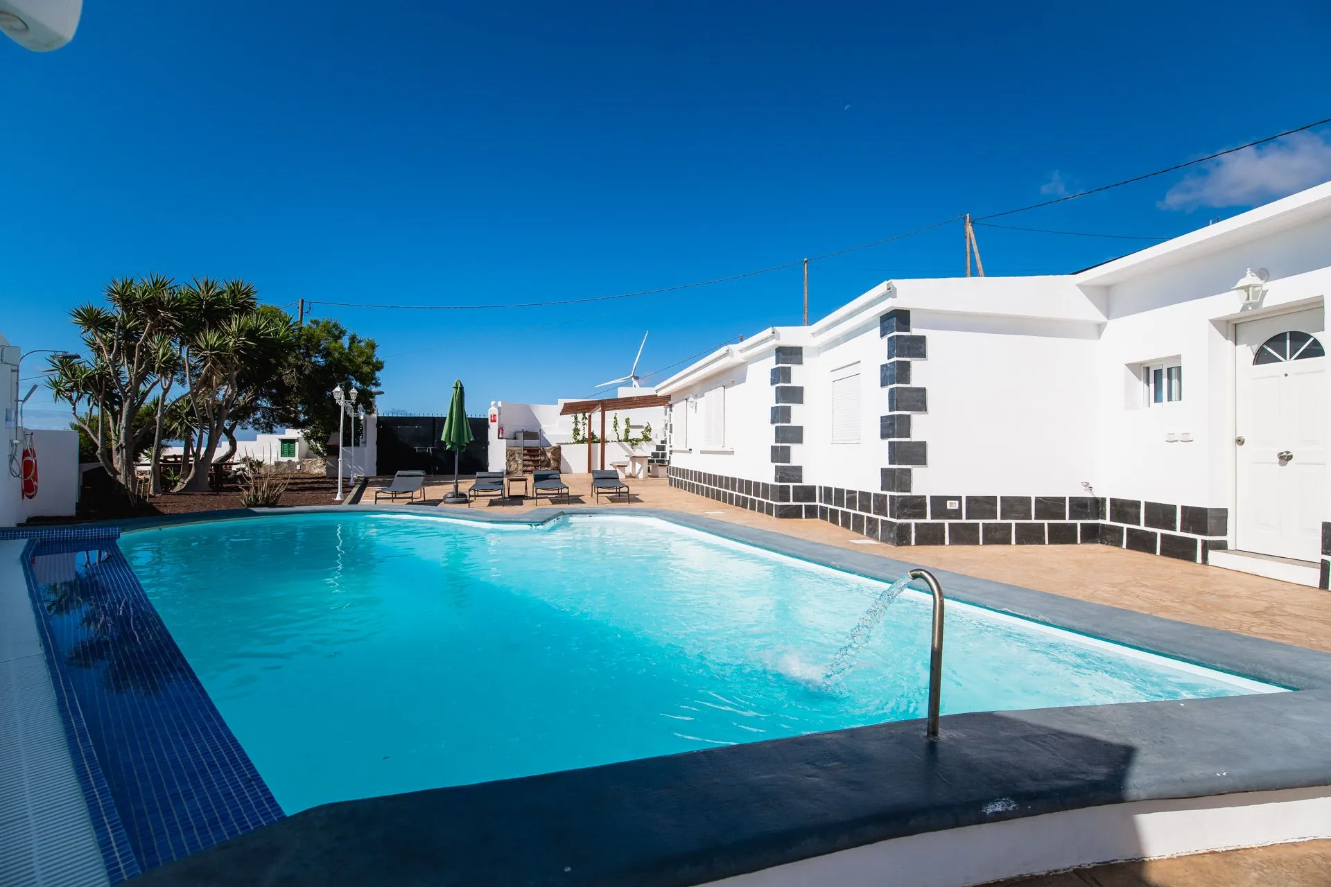 Piscina turchese con edificio bianco e mulino a vento sotto un cielo azzurro