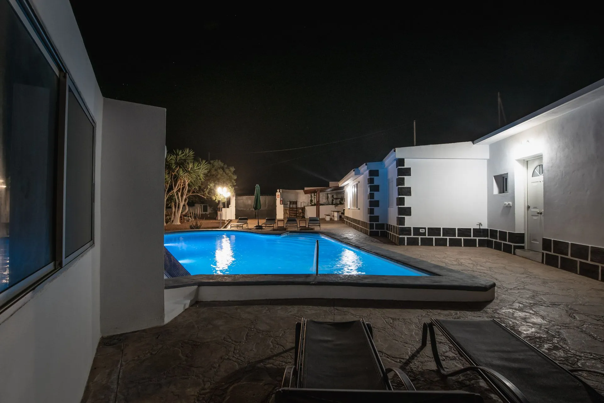 Piscina illuminata di notte con lettini scuri in primo piano