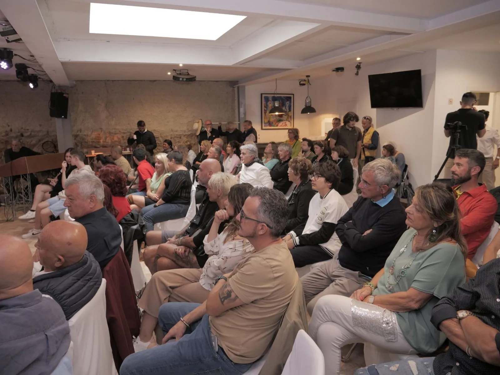 Pubblico numeroso seduto durante una presentazione in sala interna