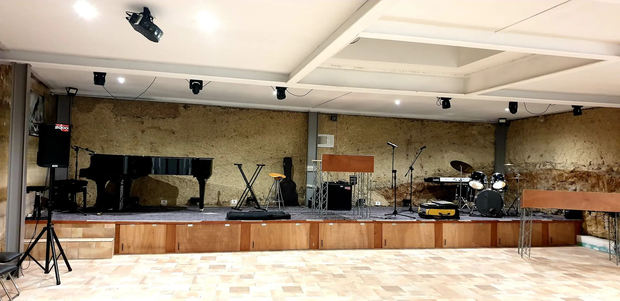 Sala concerti con palco in legno, pianoforte a coda e batteria su pareti in pietra