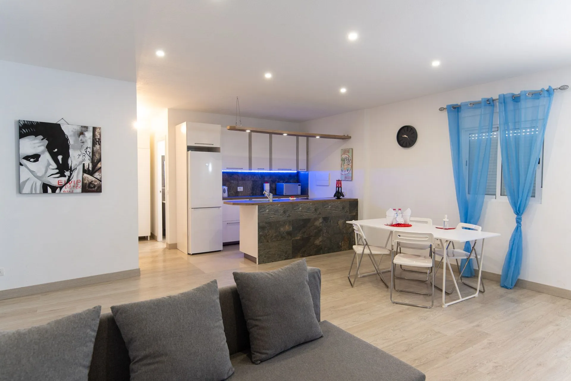 Soggiorno open space con divano grigio, tavolo e cucina bianca a Casa Genesis