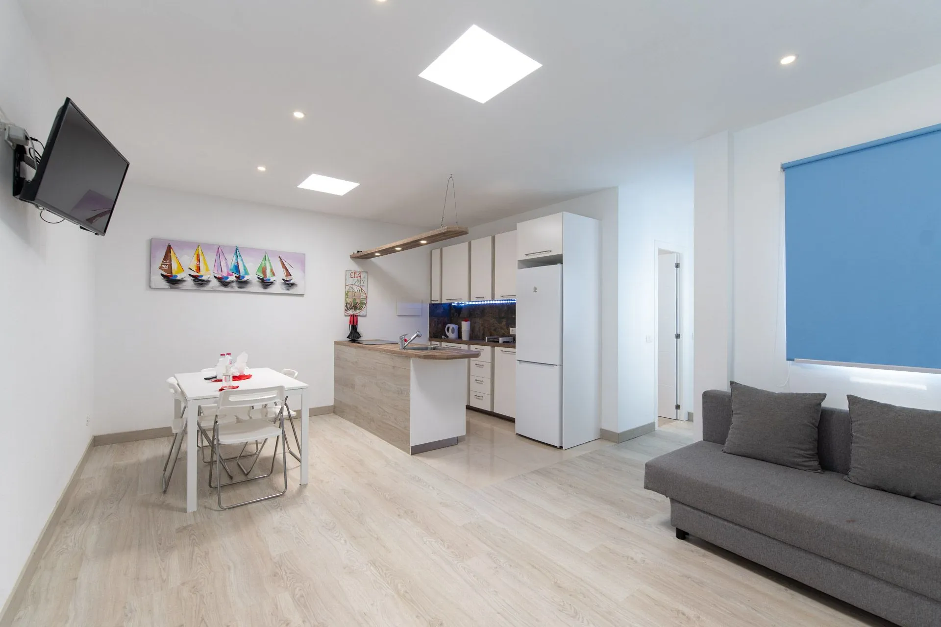 Soggiorno con cucina a vista, tenda blu e tavolo bianco a Casa Gabriel